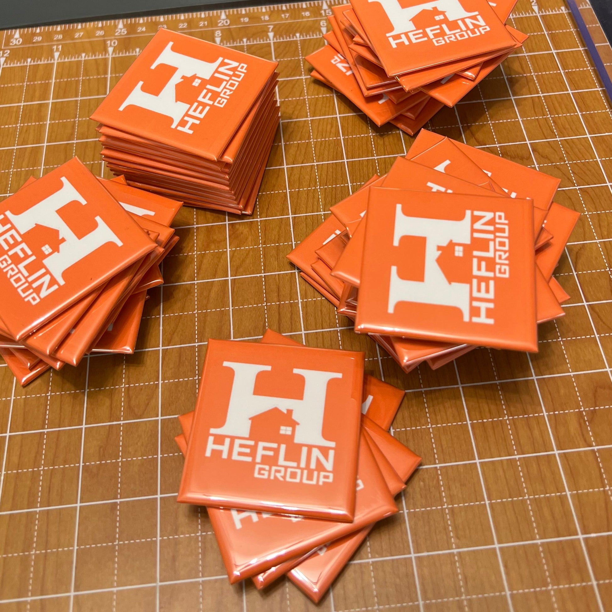 Stacks of orange stickers with 'Heflin Group' logo on a cutting mat with Trim Air logo.