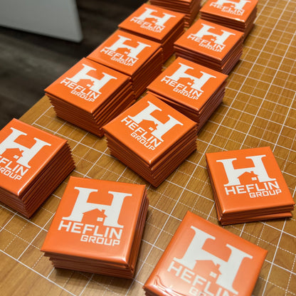 Stacks of orange stickers with 'Heflin Group' logo on a cutting mat.