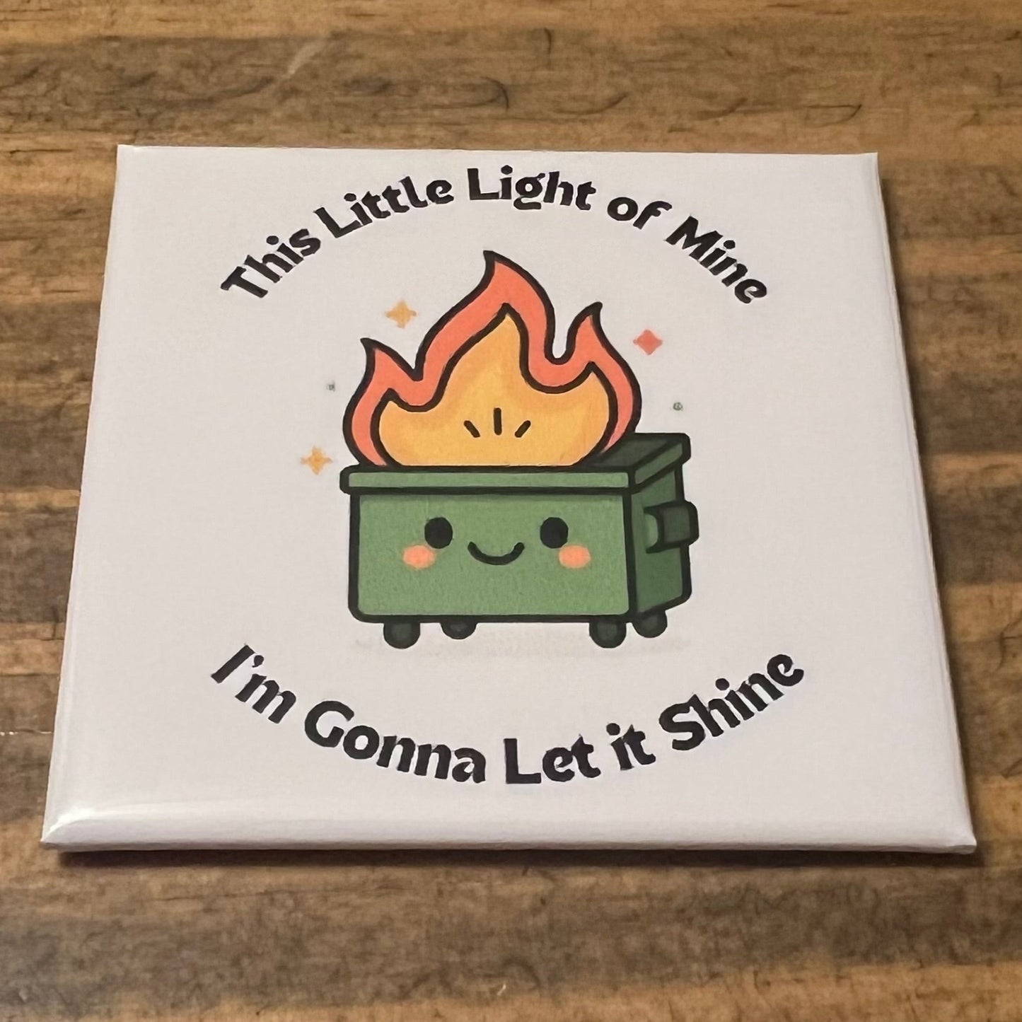 Square magnet with a cartoon fire and text on a wooden surface