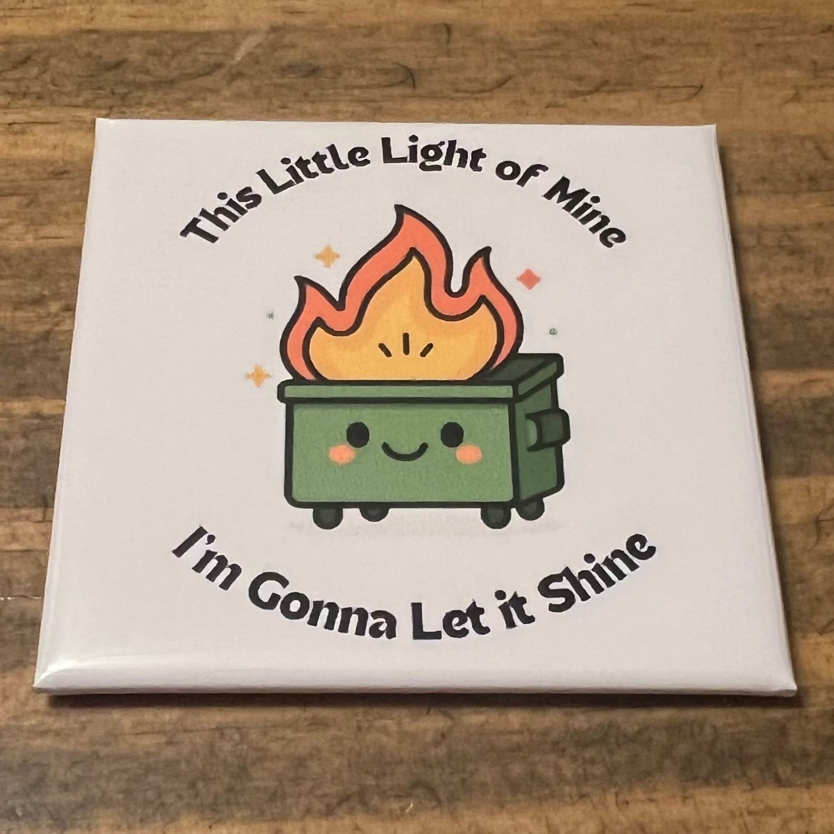 Square magnet with a cartoon fire and text on a wooden surface